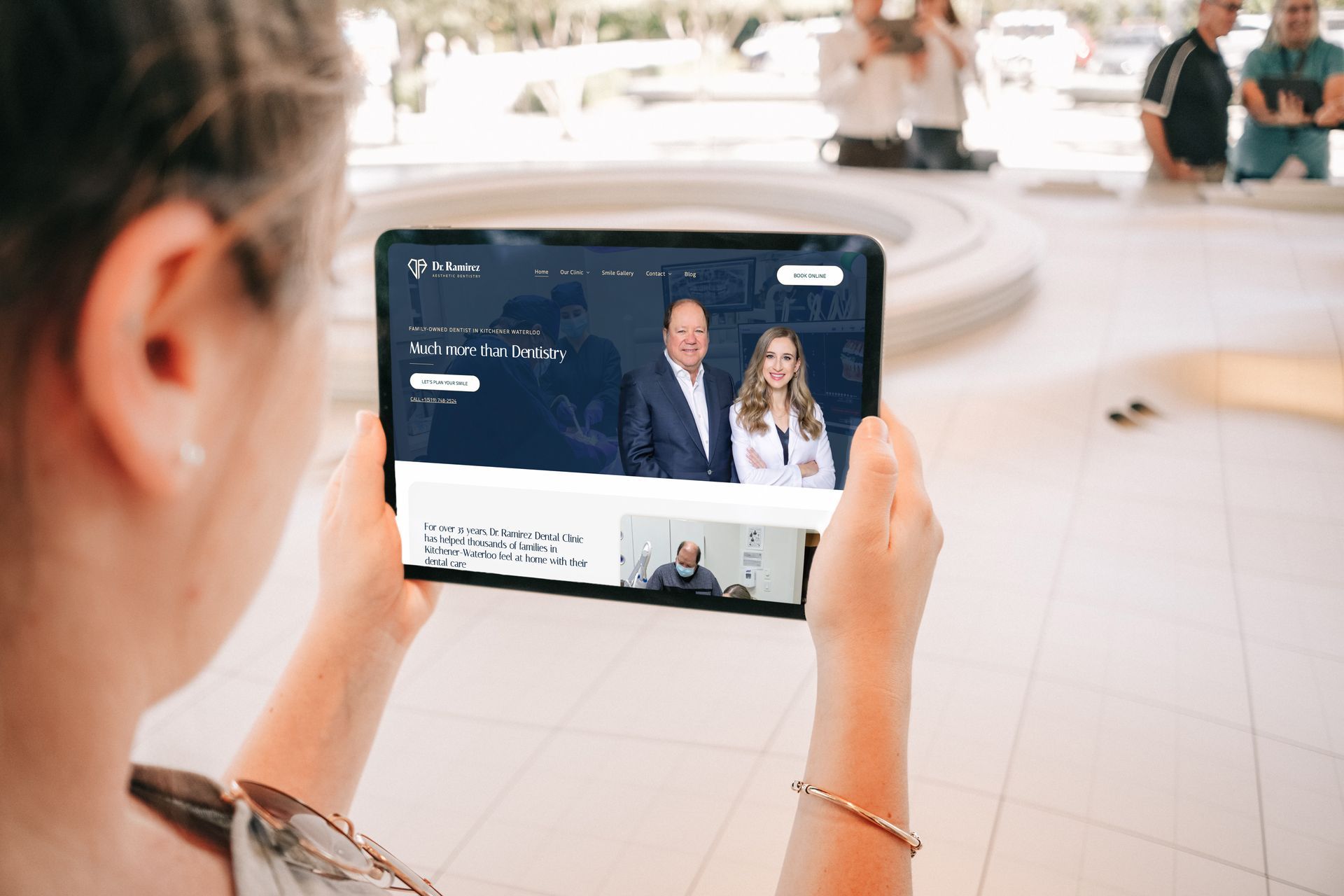 Woman holding tablet showing website with two people and text.