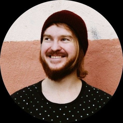 A person wearing a beige sweater and beanie kisses a Boston Terrier in a matching yellow knit sweater against orange.