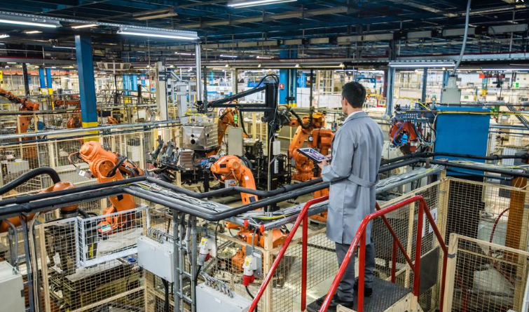 a man in a lab coat is standing in a factory looking at robots
