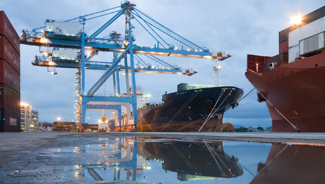 a large ship is docked at a port with cranes and containers .