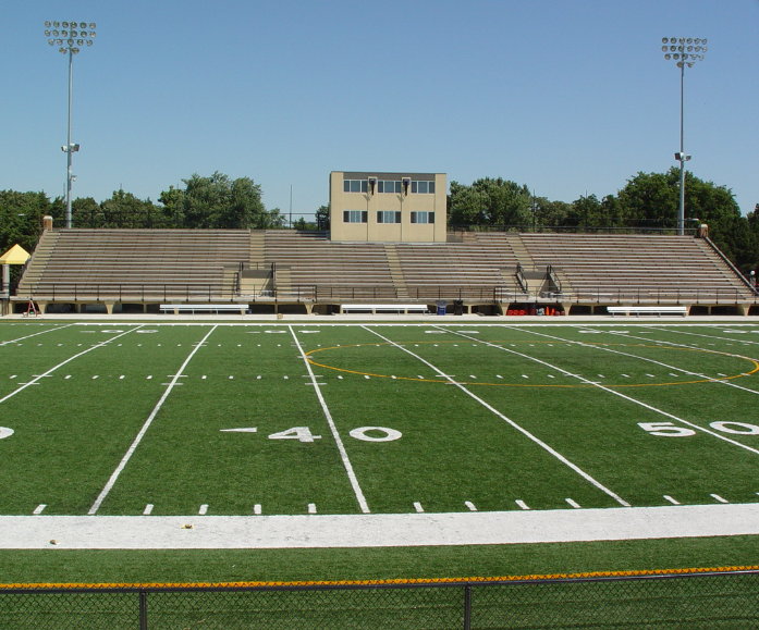 an empty football field with a stadium in the background