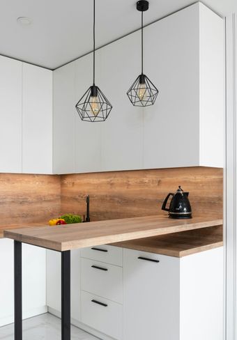 A modern kitchen with white cabinets, a wooden countertop, and black geometric pendant lights.