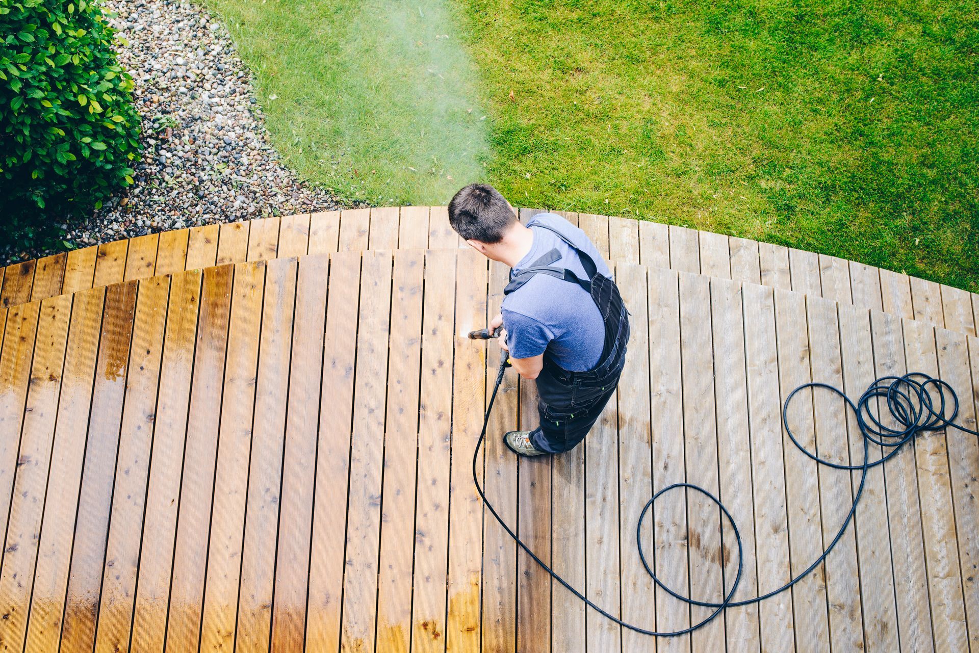 A man is cleaning a wooden deck with a high pressure washer.