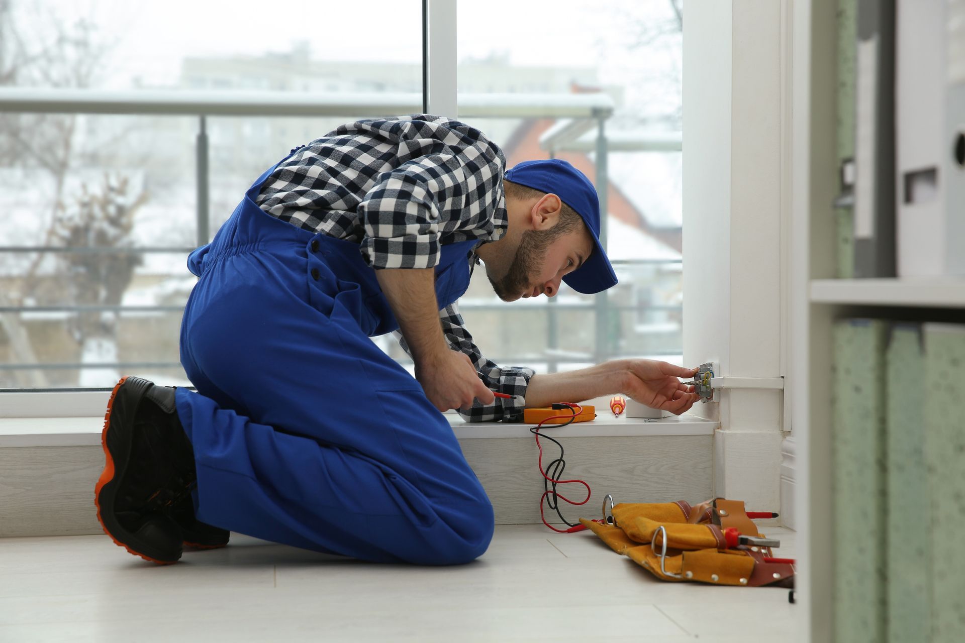 A man is kneeling on the floor fixing a light switch.