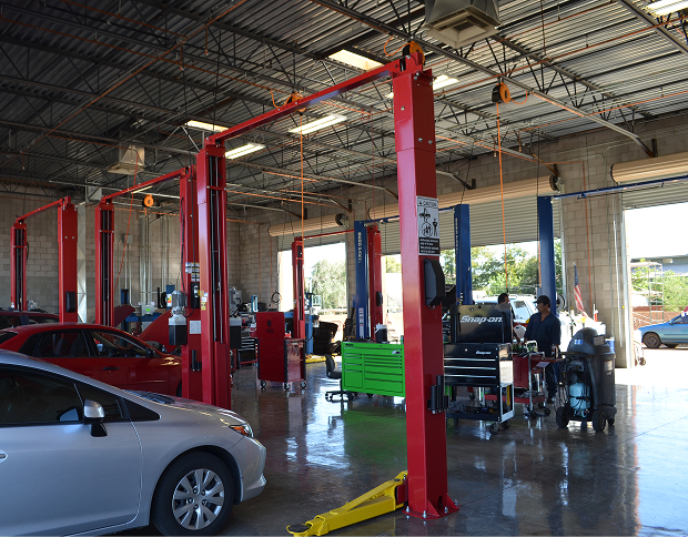 An auto repair shop interior with several red hydraulic lifts, cars, tools, and equipment on a polished concrete floor. | Japanese Auto Pros