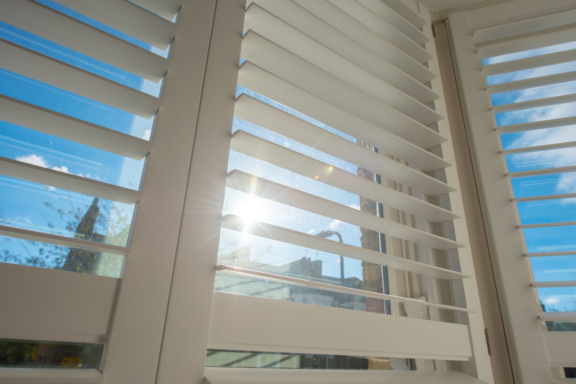 White window shutters partially blocking bright sunlight streaming through.