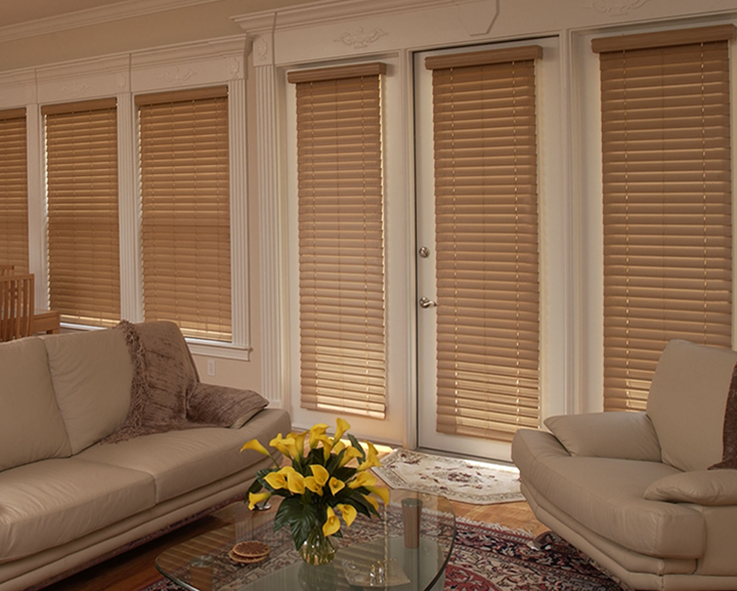 Living room with beige leather sofas, wooden blinds, and yellow flowers on a glass table.