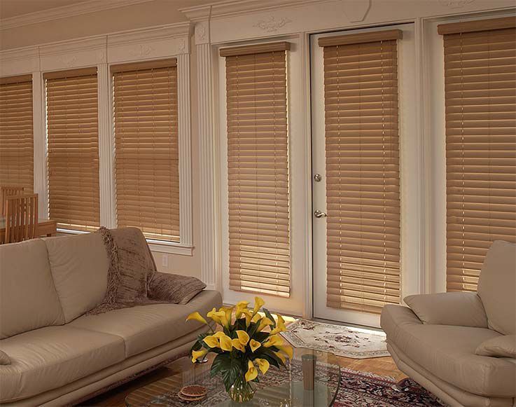A living room with beige wood blinds, a beige couch, and a sunny yellow flower arrangement.