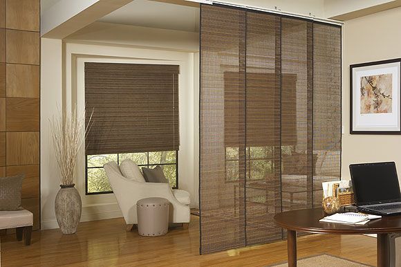 Room divider made of woven blinds, separating a window with blinds, chair, and table with laptop.