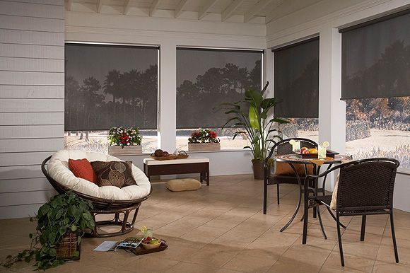 Sunroom with black blinds, patio furniture, plants, and view of trees.