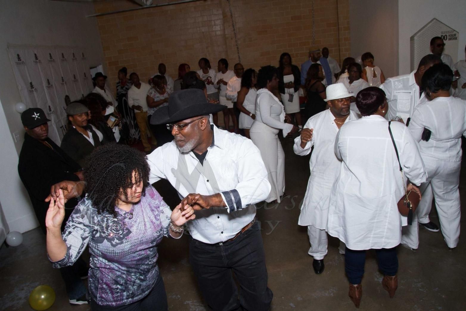 People dancing in a crowded indoor party, with a couple in the foreground under dim lighting