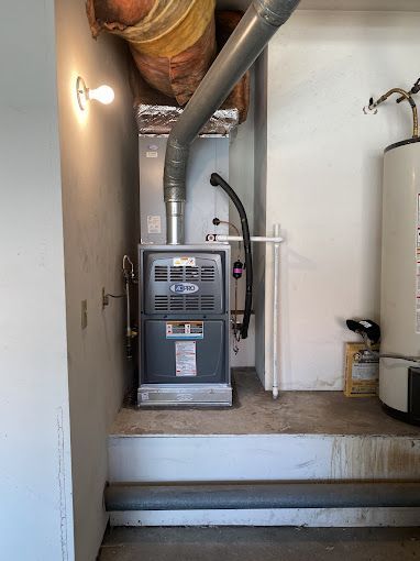 A furnace is sitting in a corner of a room next to a water heater.