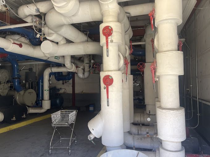 A shopping cart is sitting in a room with lots of pipes