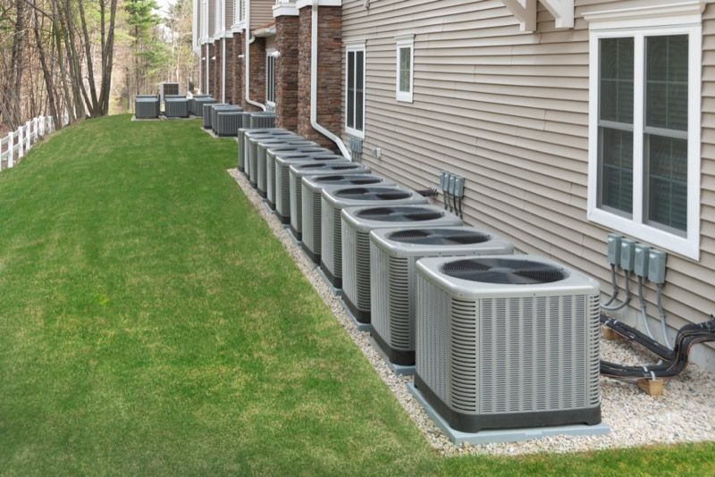 A row of air conditioners are lined up on the side of a house.