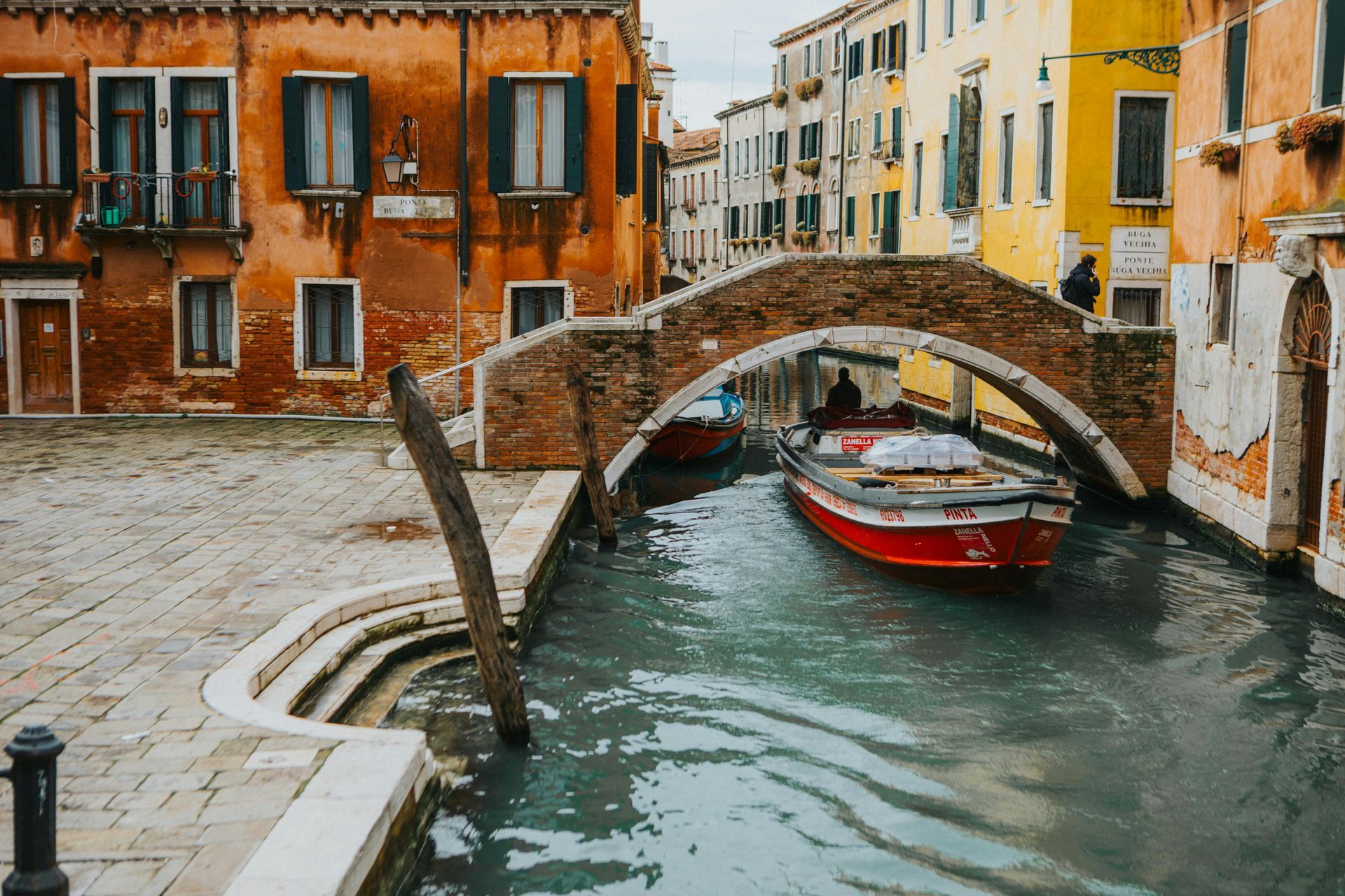 A boat is going under a bridge in a canal in venice.