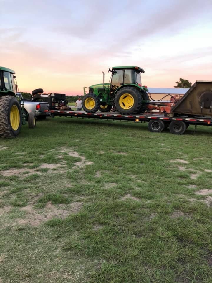 A tractor is being towed by a trailer in a grassy field.