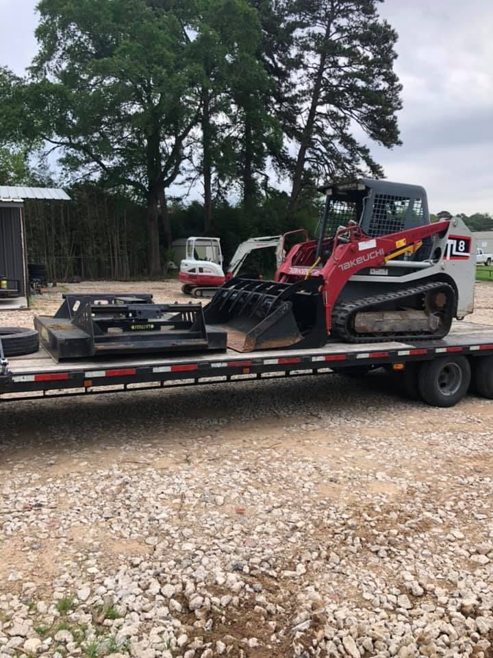 A bulldozer is sitting on top of a trailer in a gravel lot.