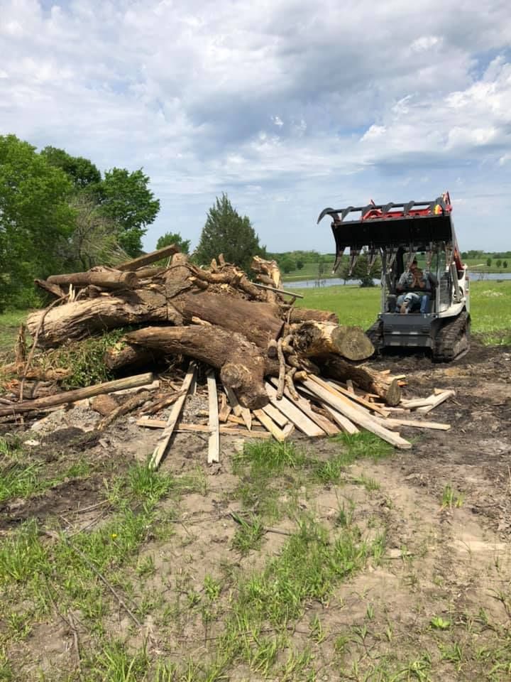 A bulldozer is moving a pile of logs in a field.