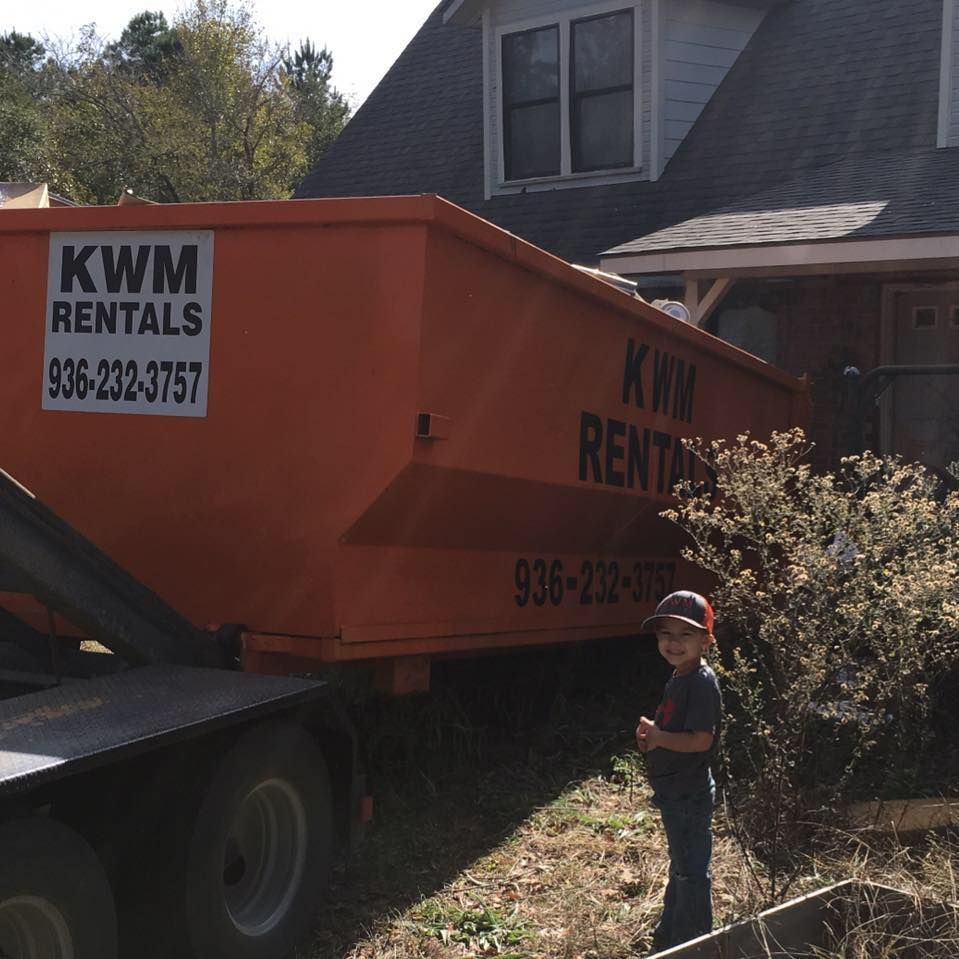 A boy stands in front of a dumpster that says kwm rentals