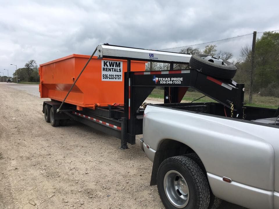 A dumpster on a trailer is being towed by a truck.