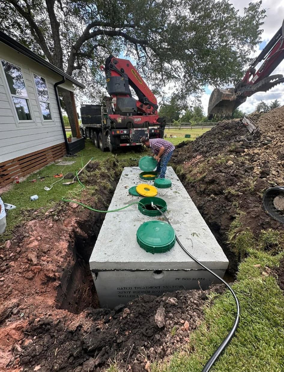 A concrete septic tank is being installed. A person works near the tank as a crane hoists equipment.