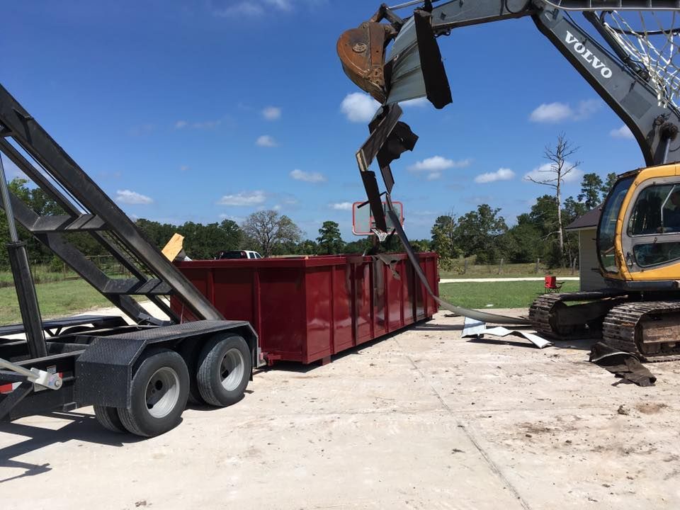 A volvo excavator is loading a dumpster onto a trailer.