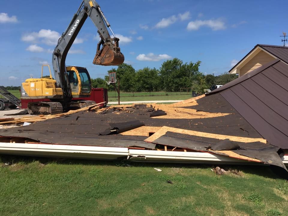 A yellow excavator is working on a roof of a house.
