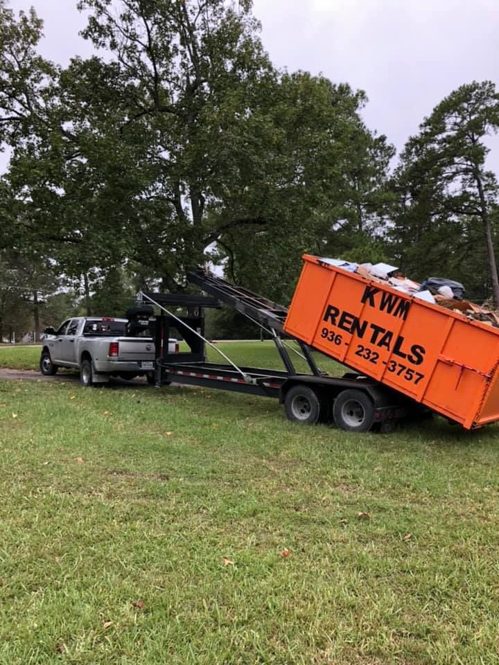 A dumpster is being pulled by a truck on a trailer.