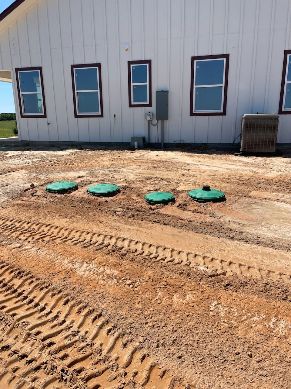 Four green septic tank covers in dirt in front of a white building with windows.