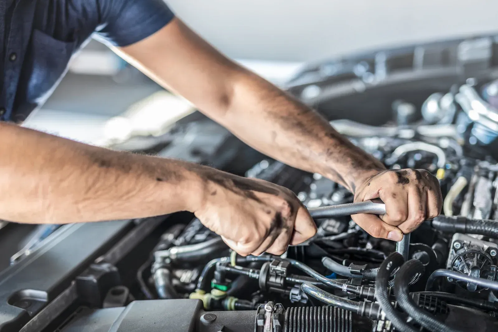 Mechanic working on car engine, using a wrench. Hands visible, in a garage.