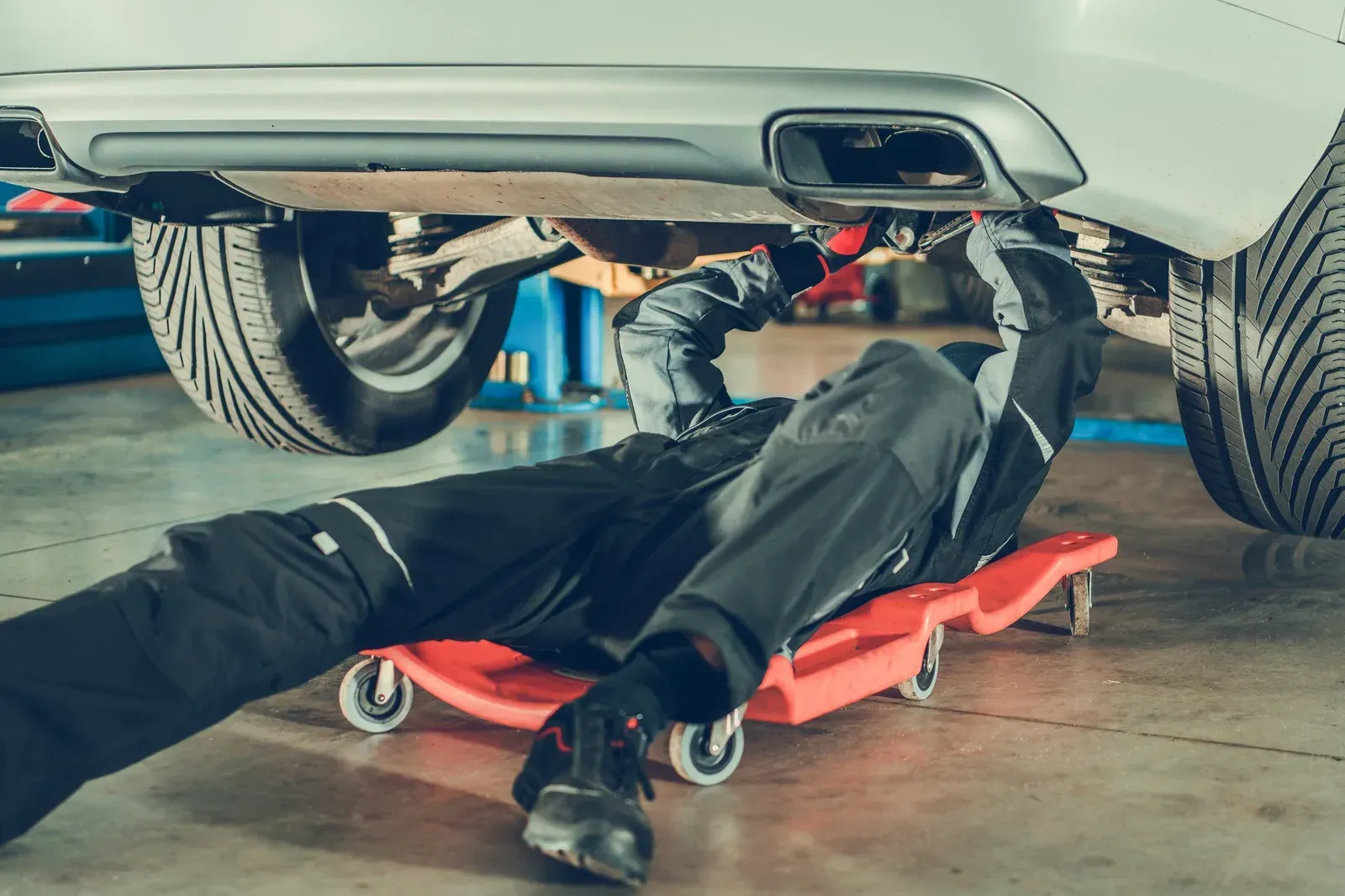 A mechanic is laying on a creeper under a car in a garage.