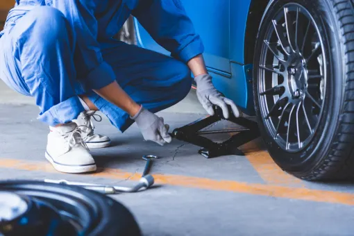 A man is changing a tire on a blue car.