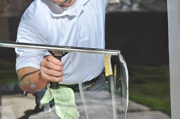 Person using a squeegee to clean a glass window, removing water with a steady motion.