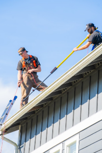 Two roofers on a house roof using safety harnesses and ropes against a blue sky