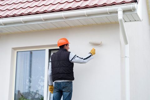 A man in gear is holding a brush to paint the outside walls.