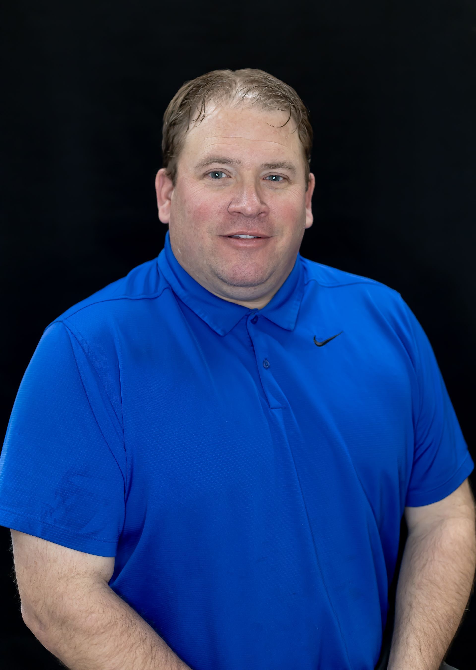 A man in a blue shirt is standing in front of a black background.