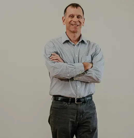 A man in a striped shirt is standing with his arms crossed and smiling