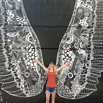 A woman is standing in front of a large mural on a wall.