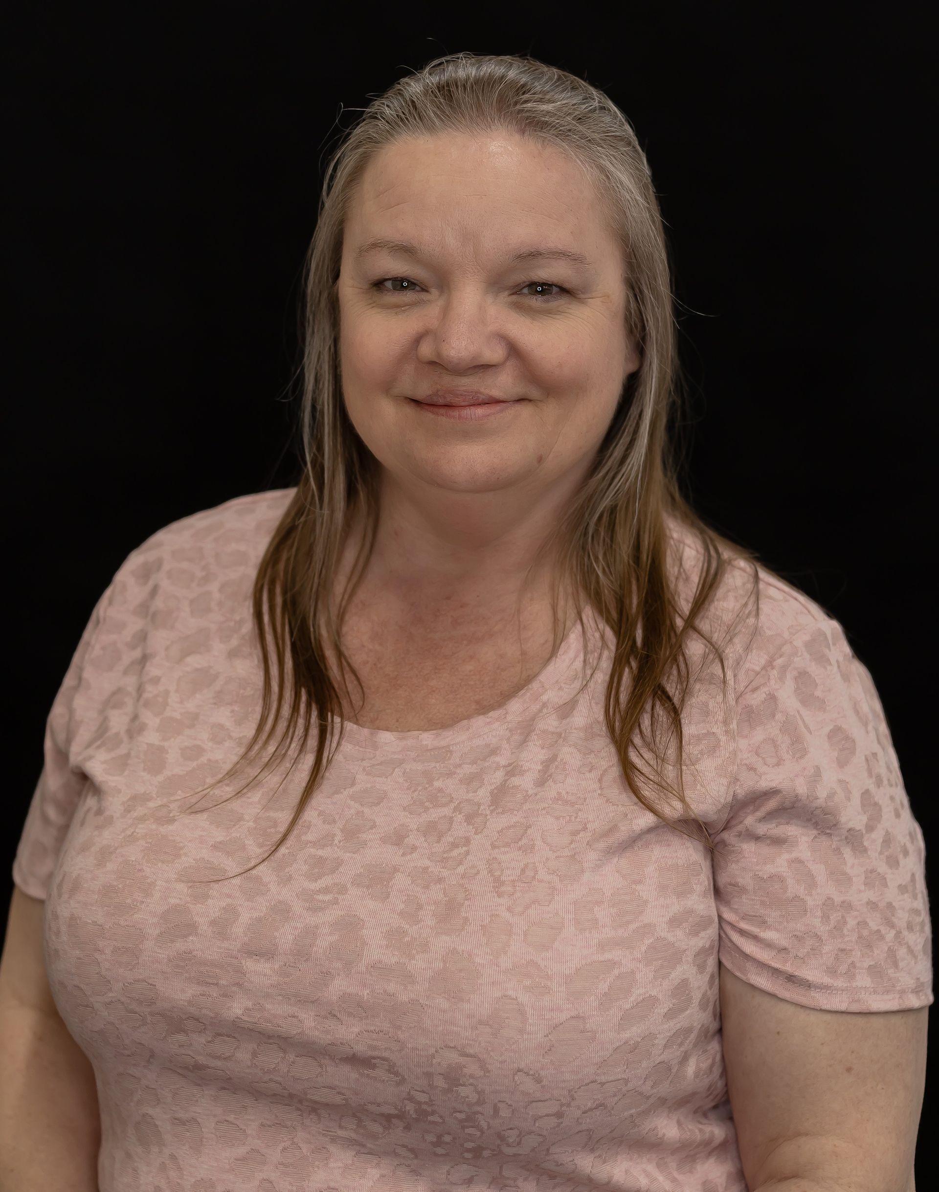 A woman in a pink shirt is smiling and wearing a headband.