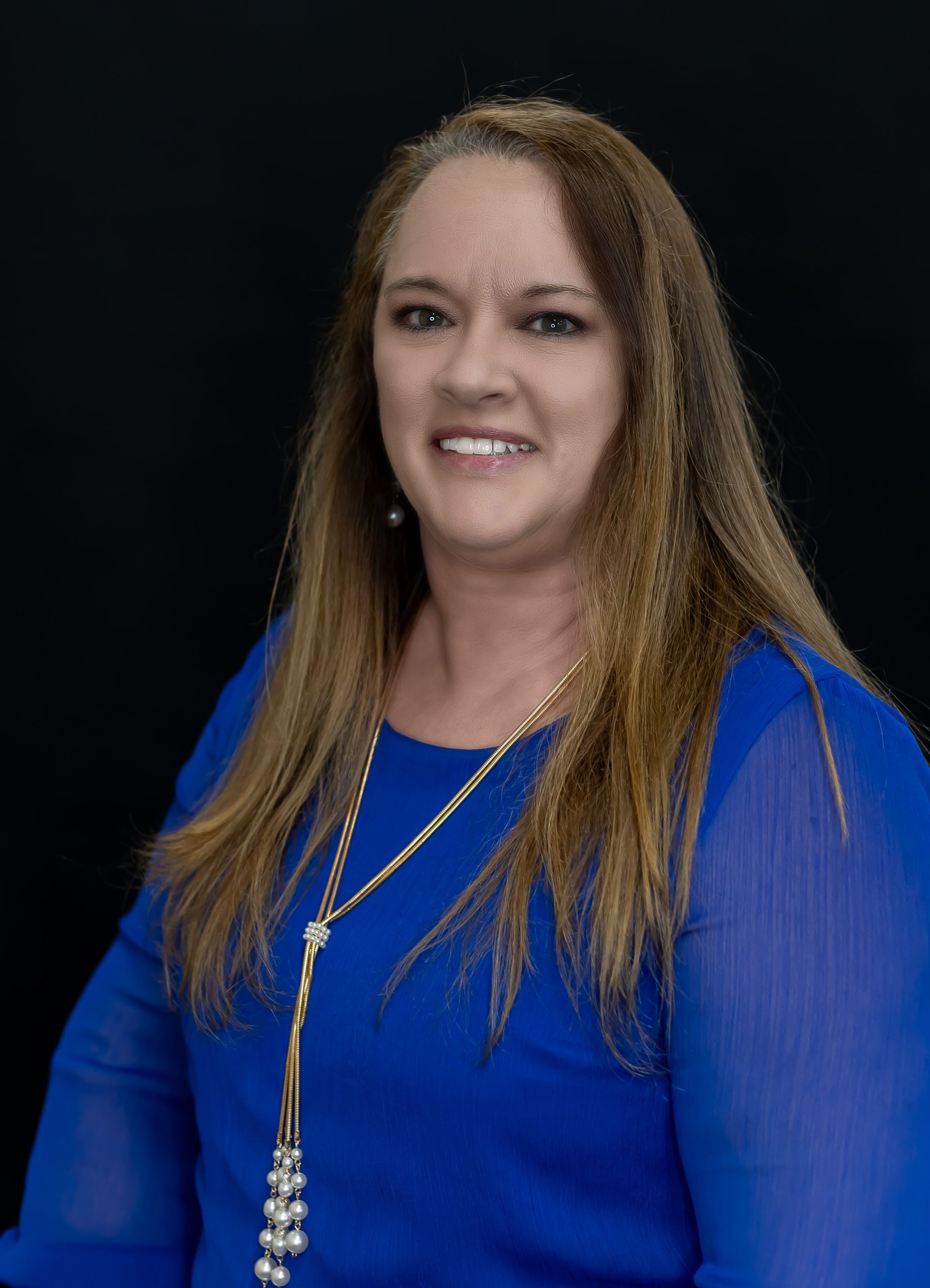 A woman is wearing a blue shirt and a gold necklace.