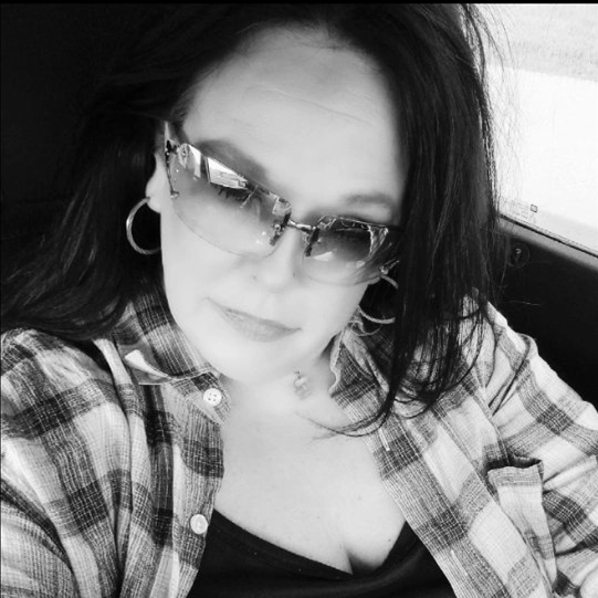 A woman wearing sunglasses and a plaid shirt is sitting in a car.