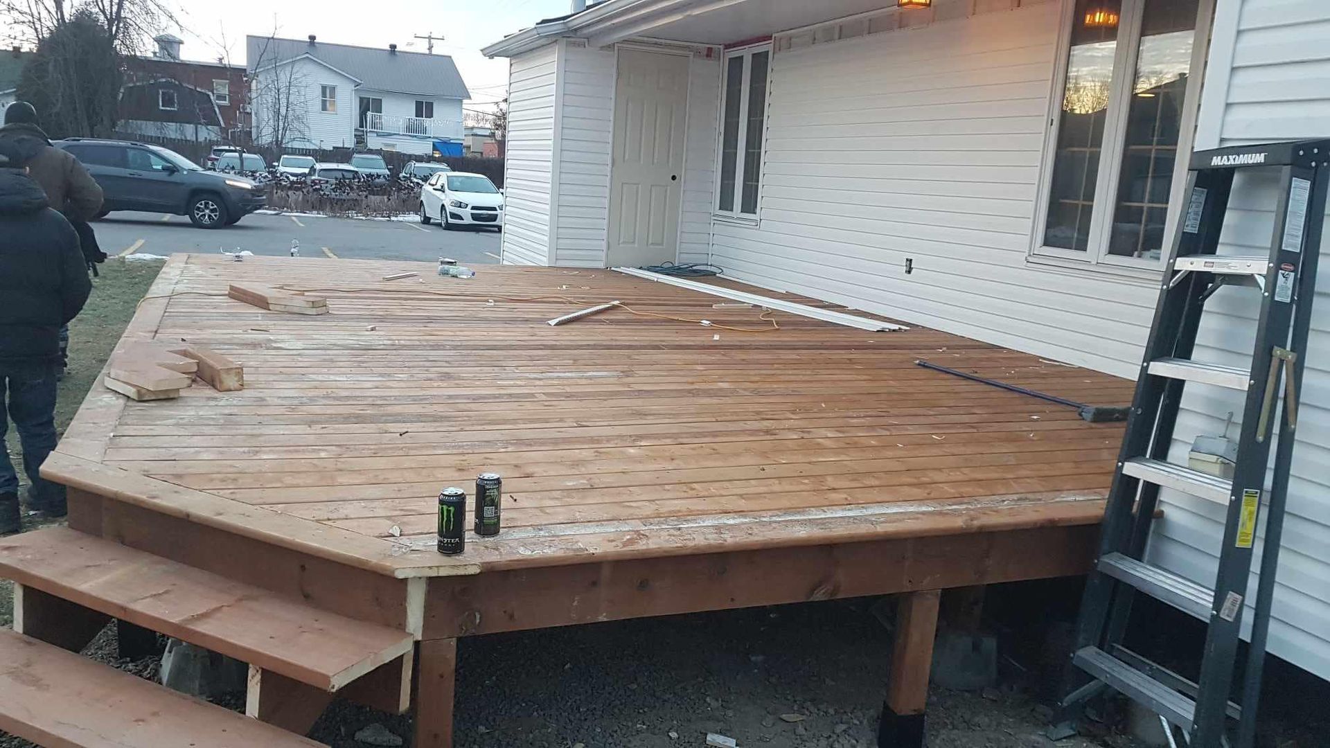 Une terrasse en bois est en construction devant une maison blanche.