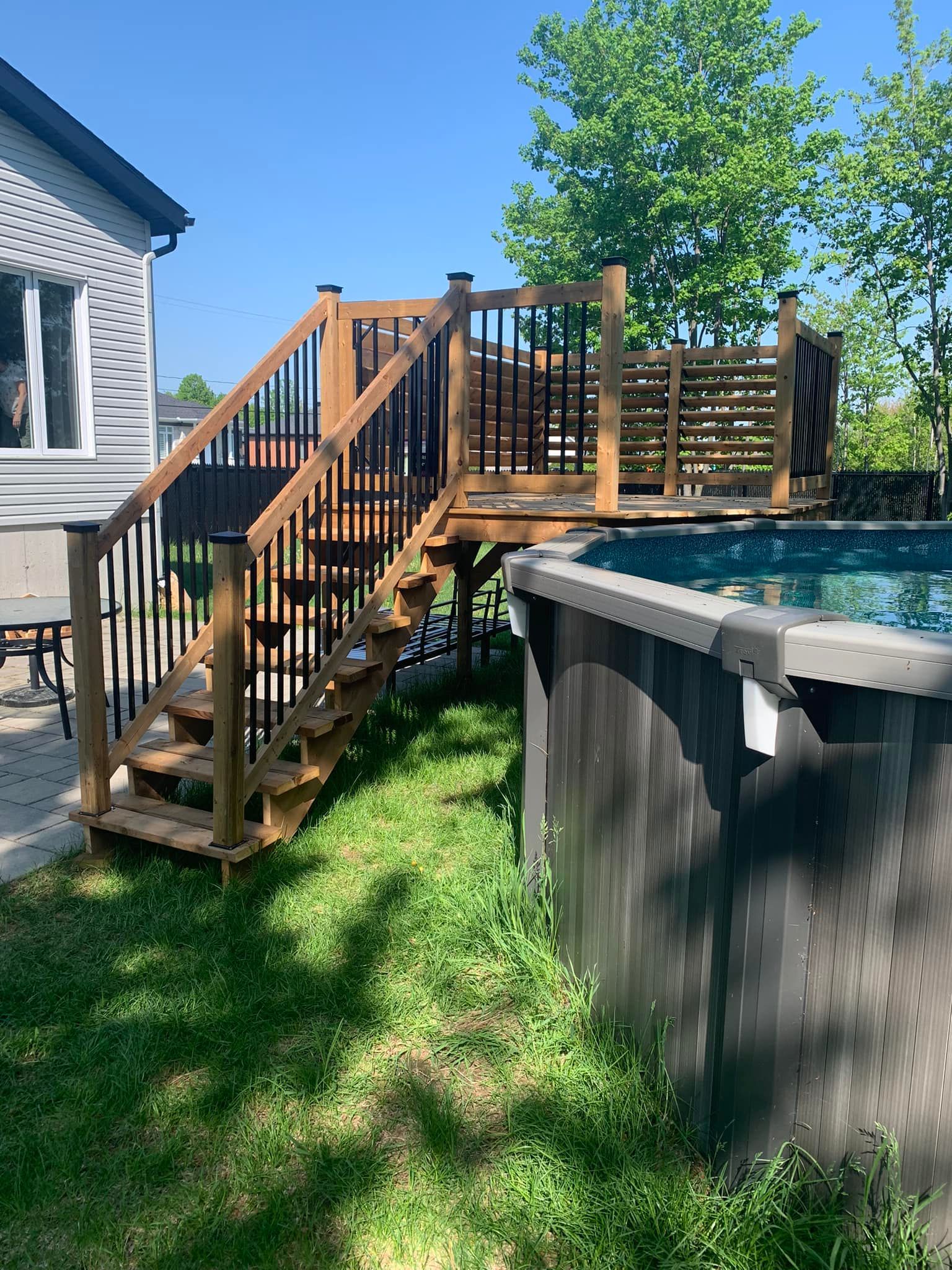 Une terrasse en bois avec des escaliers qui y mènent à côté d'une piscine.