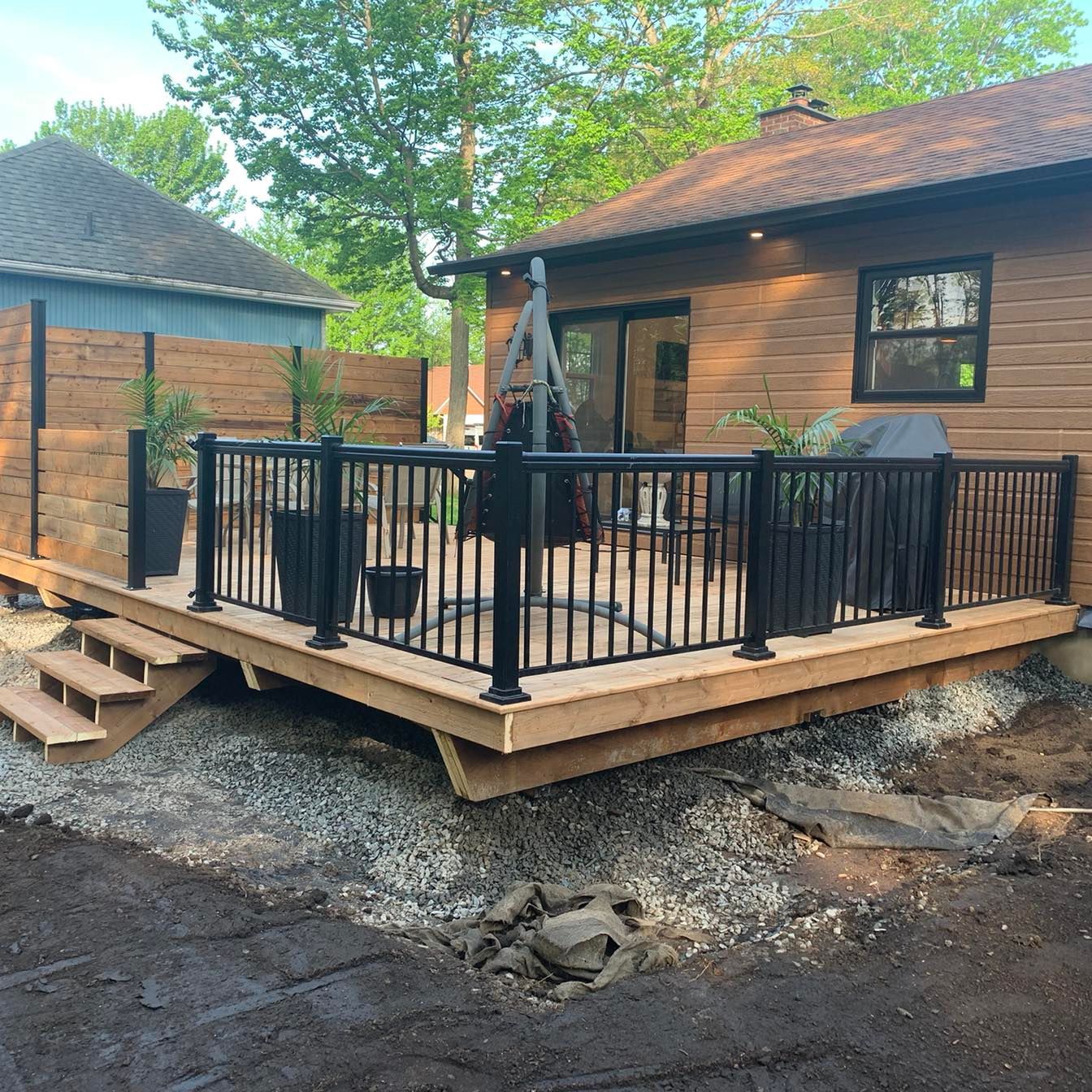 Une terrasse en bois avec une balustrade noire se trouve devant une maison.