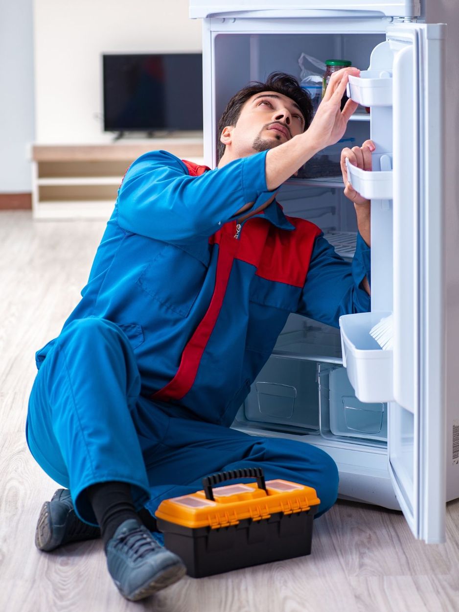 Two men are working on a refrigerator in a kitchen.