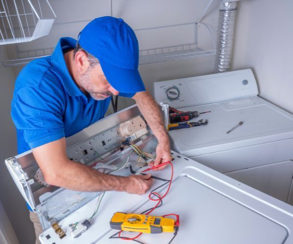 A man in a blue shirt is working on a washer and dryer