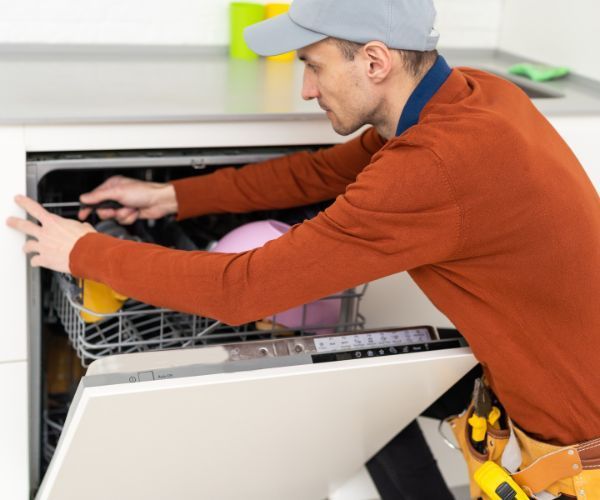 A man is working on a dishwasher in a kitchen