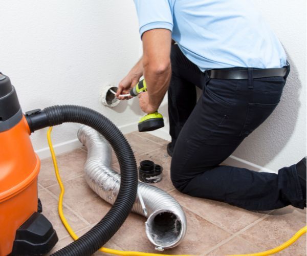 A man is kneeling down next to a vacuum cleaner and a hose.