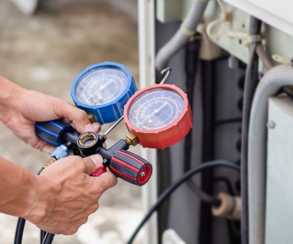 A man is working on an air conditioner with two gauges.