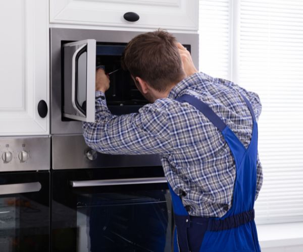 A man is fixing a microwave oven in a kitchen.